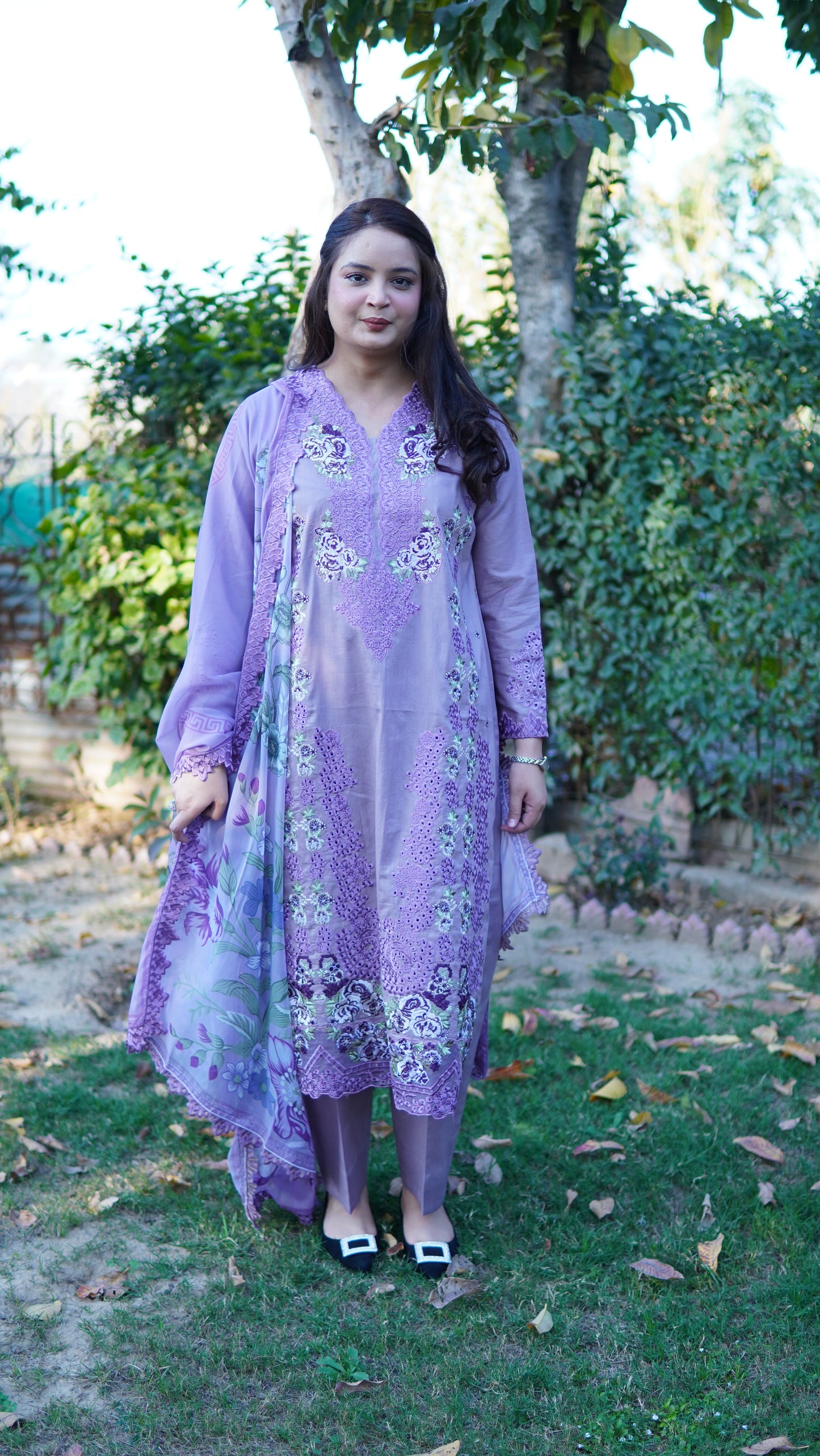 Woman wearing a purple floral dress standing outdoors with trees in the background